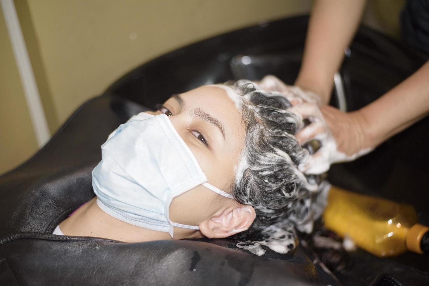 a young woman is getting a haircut in a hair salon , wearing face mask for protection covid-19 , salon safety concept photo
