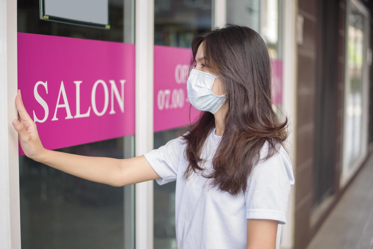 a young woman is wearing face mask for protection covid-19 standing in front of Salon shop, salon safety concept photo