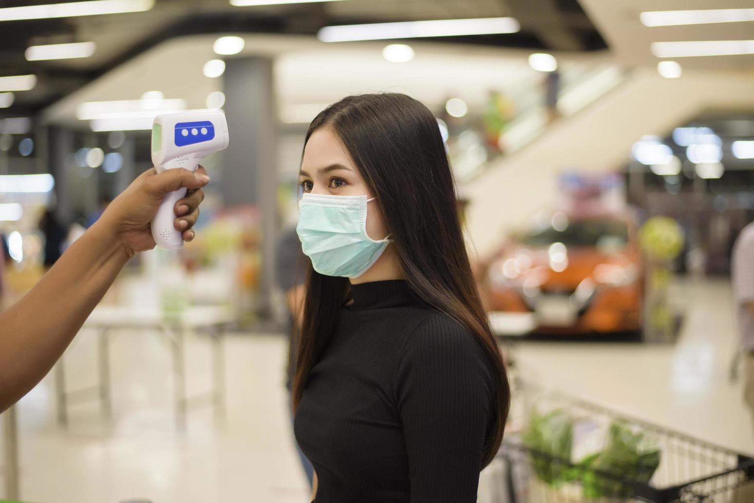 Close up hand Using temperature gun with young woman , social distancing measure for COVID-19 prevention in shopping center photo