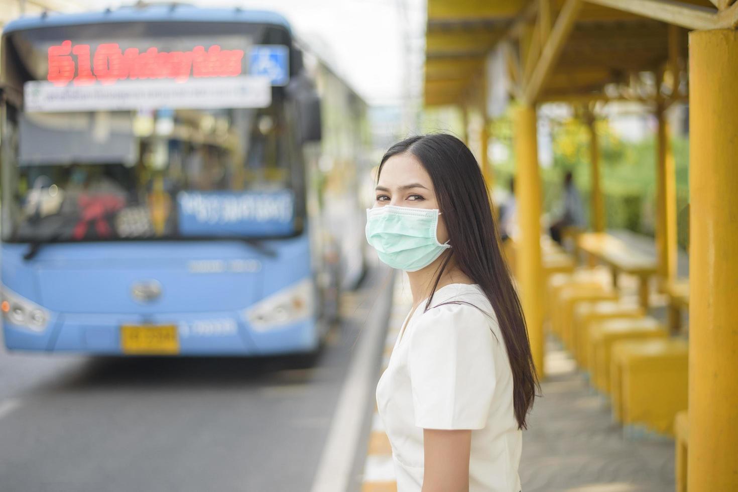 bella mujer lleva mascarilla en la parada de autobús foto