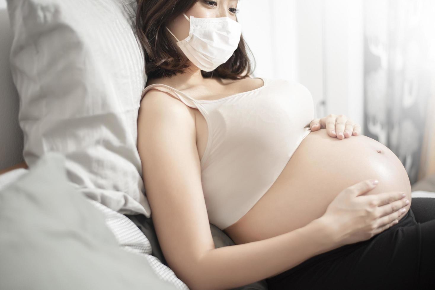 bella mujer asiática embarazada lleva una máscara protectora en su casa, concepto de protección contra el coronavirus foto