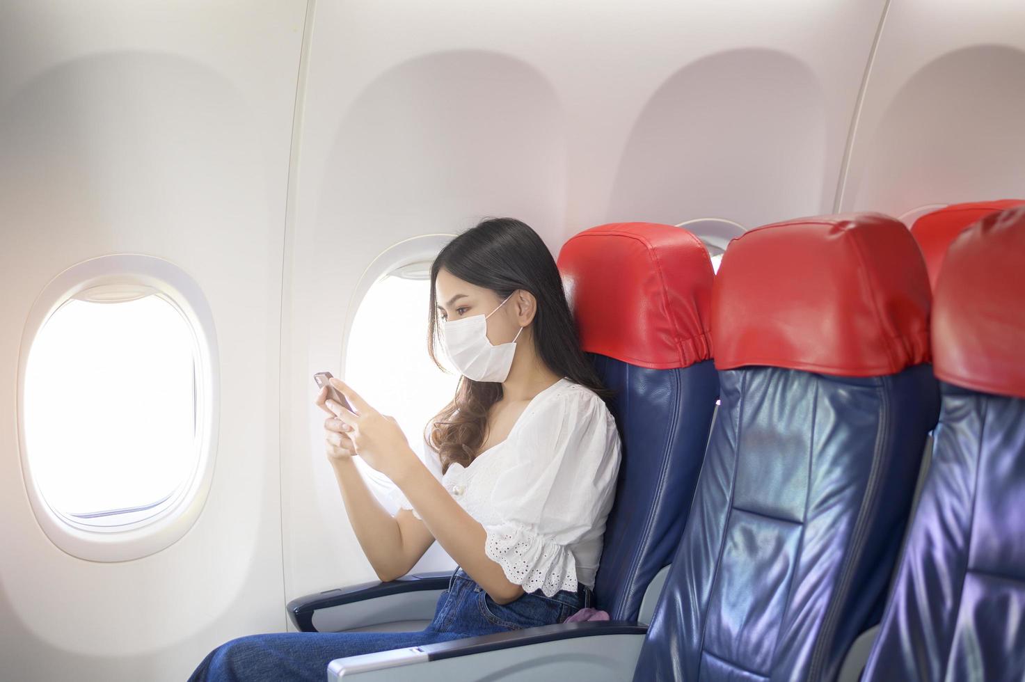 A young woman wearing face mask is using smartphone onboard, New normal travel after covid-19 pandemic concept photo