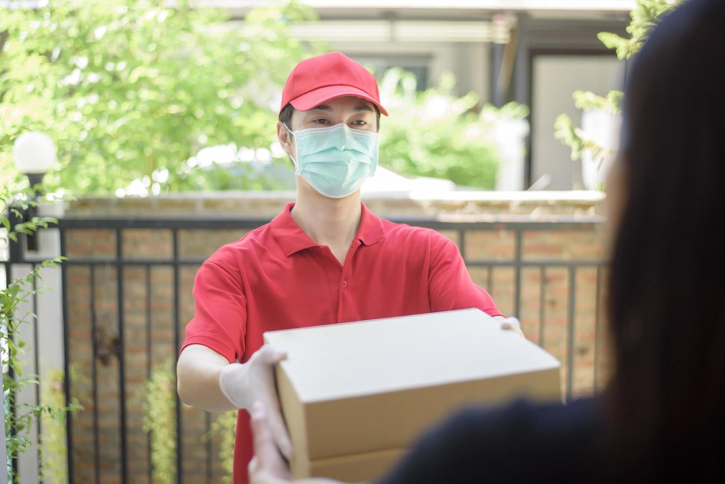 el mensajero con máscara protectora y guantes entrega alimentos en caja durante el brote de virus. entrega segura a domicilio. foto