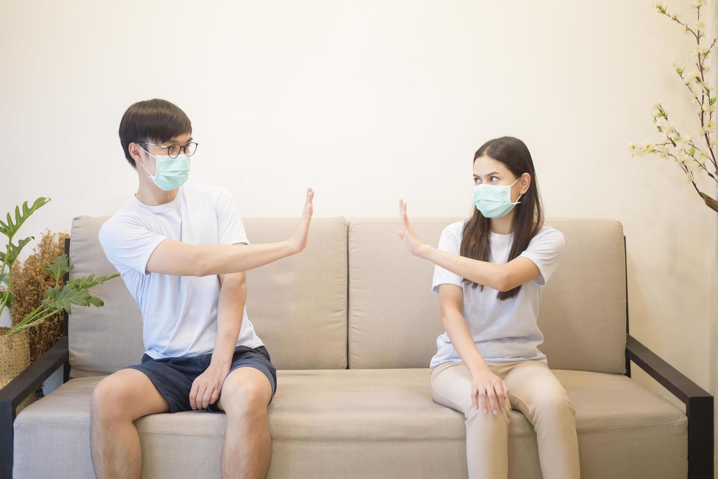 A couple wearing a mask is sitting on a sofa at home during quarantine for protection and avoiding from coronavirus photo