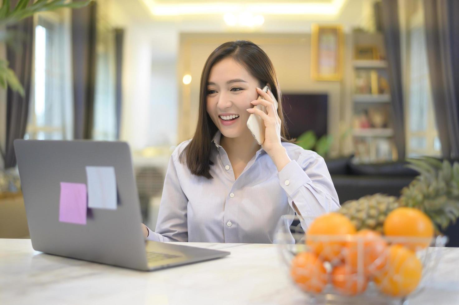 una hermosa mujer de negocios asiática está trabajando con su computadora en casa, telecomunicaciones, distanciamiento social, concepto de trabajo desde casa foto