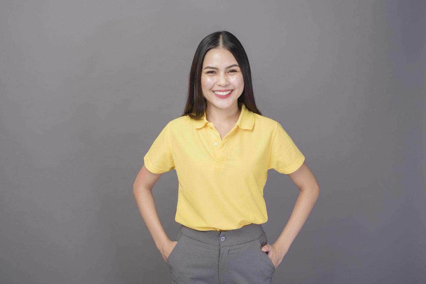 joven mujer hermosa y segura de sí misma con camisa amarilla está en un estudio de fondo gris foto