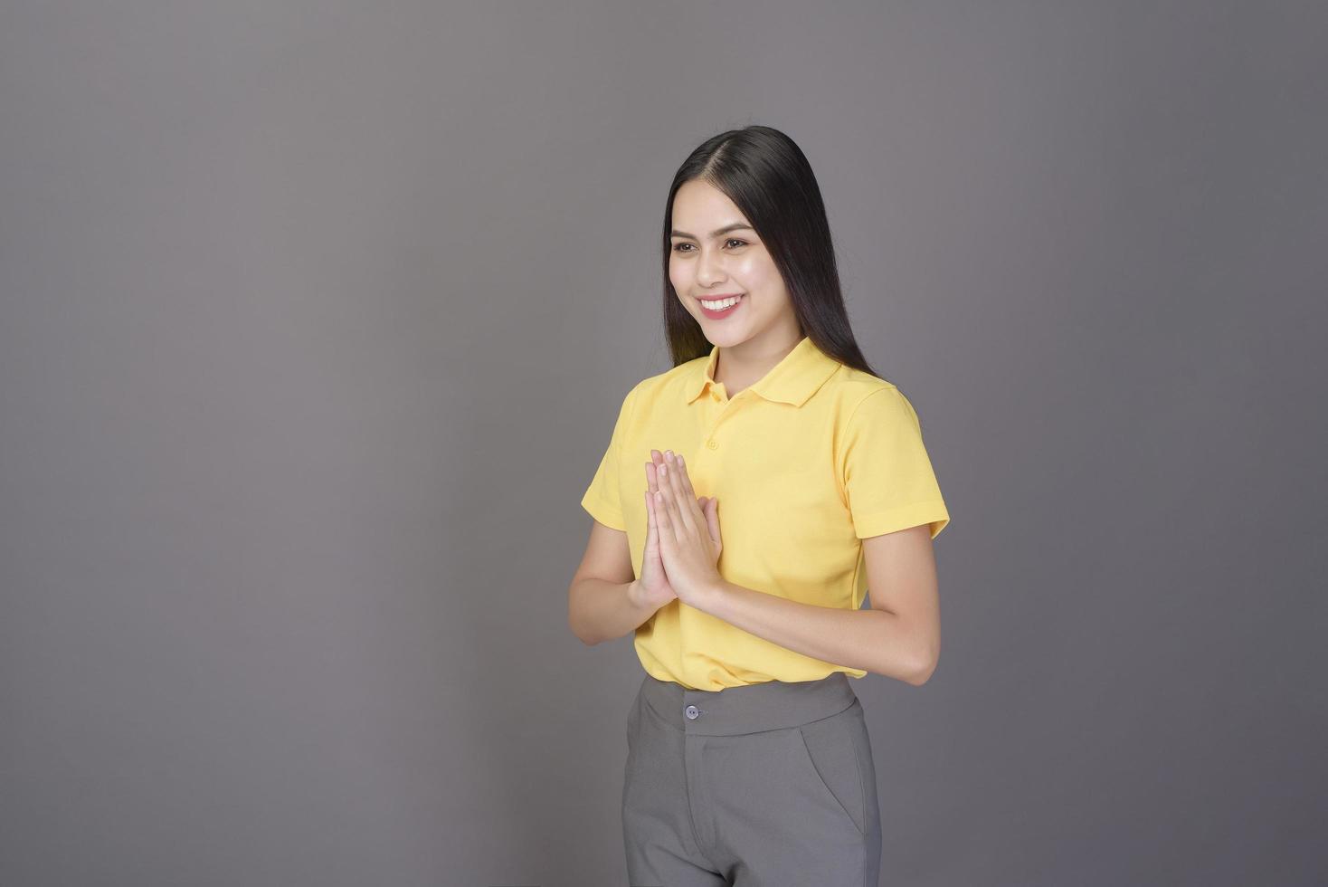 beautiful confident woman is greeting Thai wai to show respect over grey background studio photo