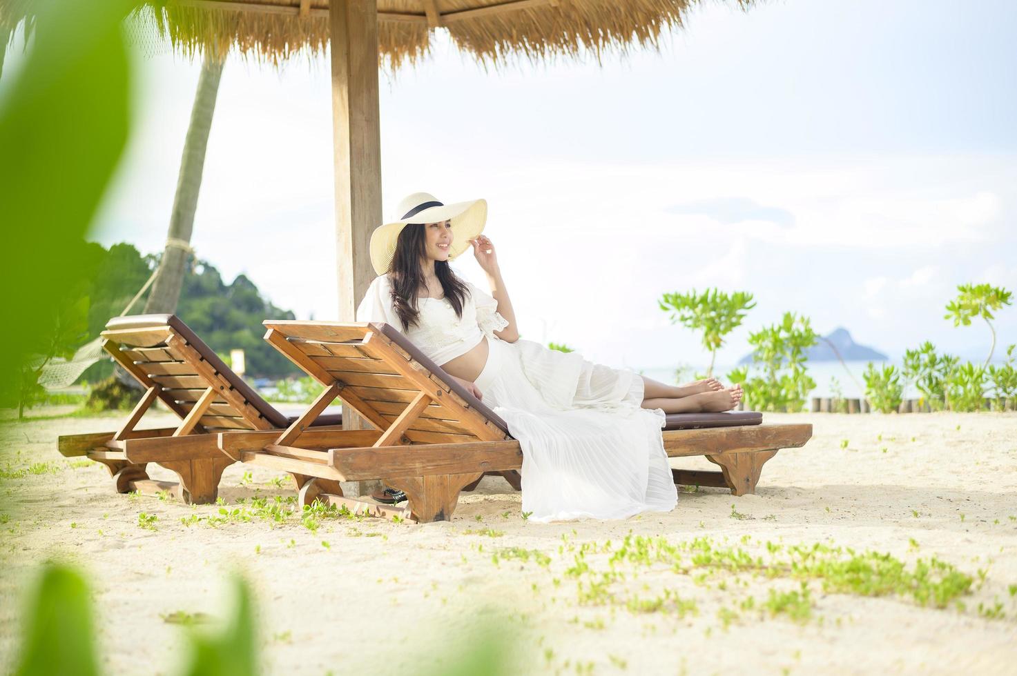 una joven relajándose y sentada en el sillón mirando la hermosa playa de vacaciones foto