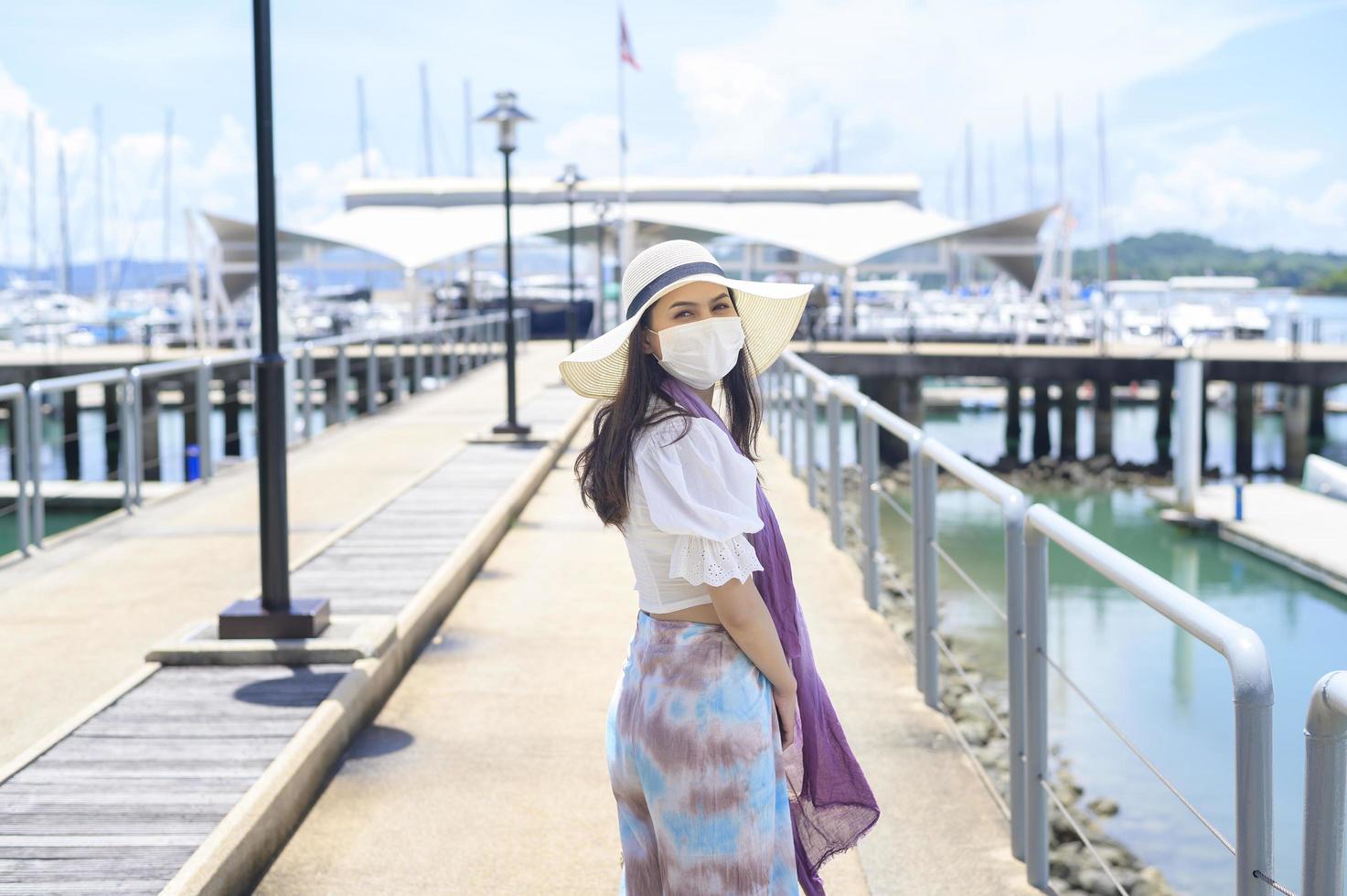 A traveller woman is wearing protective mask in on the dock, travel under Covid-19 pandemic, safety travels, social distancing protocol, New normal travel concept photo