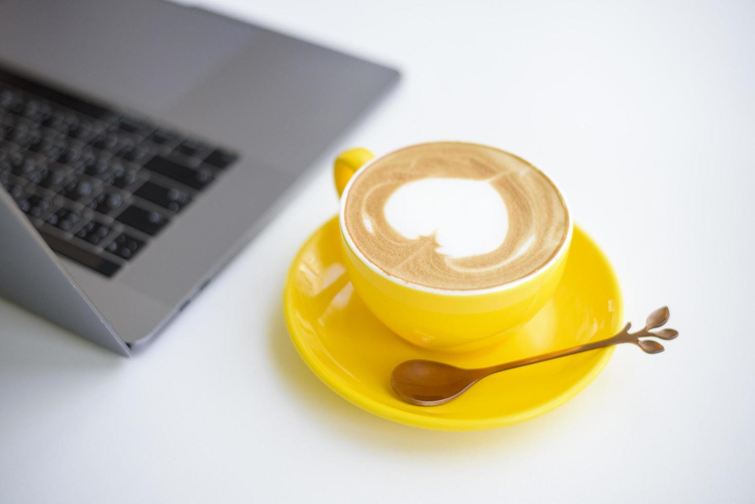 arte latte caliente en taza amarilla en el escritorio de trabajo foto