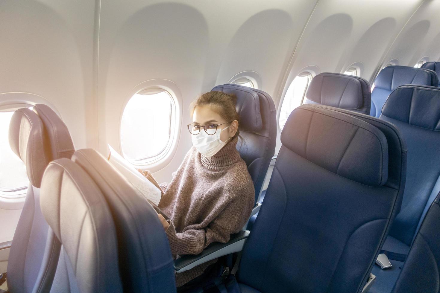 una mujer joven con mascarilla viaja en avión, nuevo viaje normal después del concepto de pandemia covid-19 foto