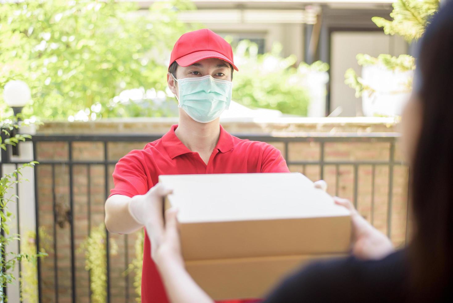 el mensajero con máscara protectora y guantes entrega alimentos en caja durante el brote de virus. entrega segura a domicilio. foto