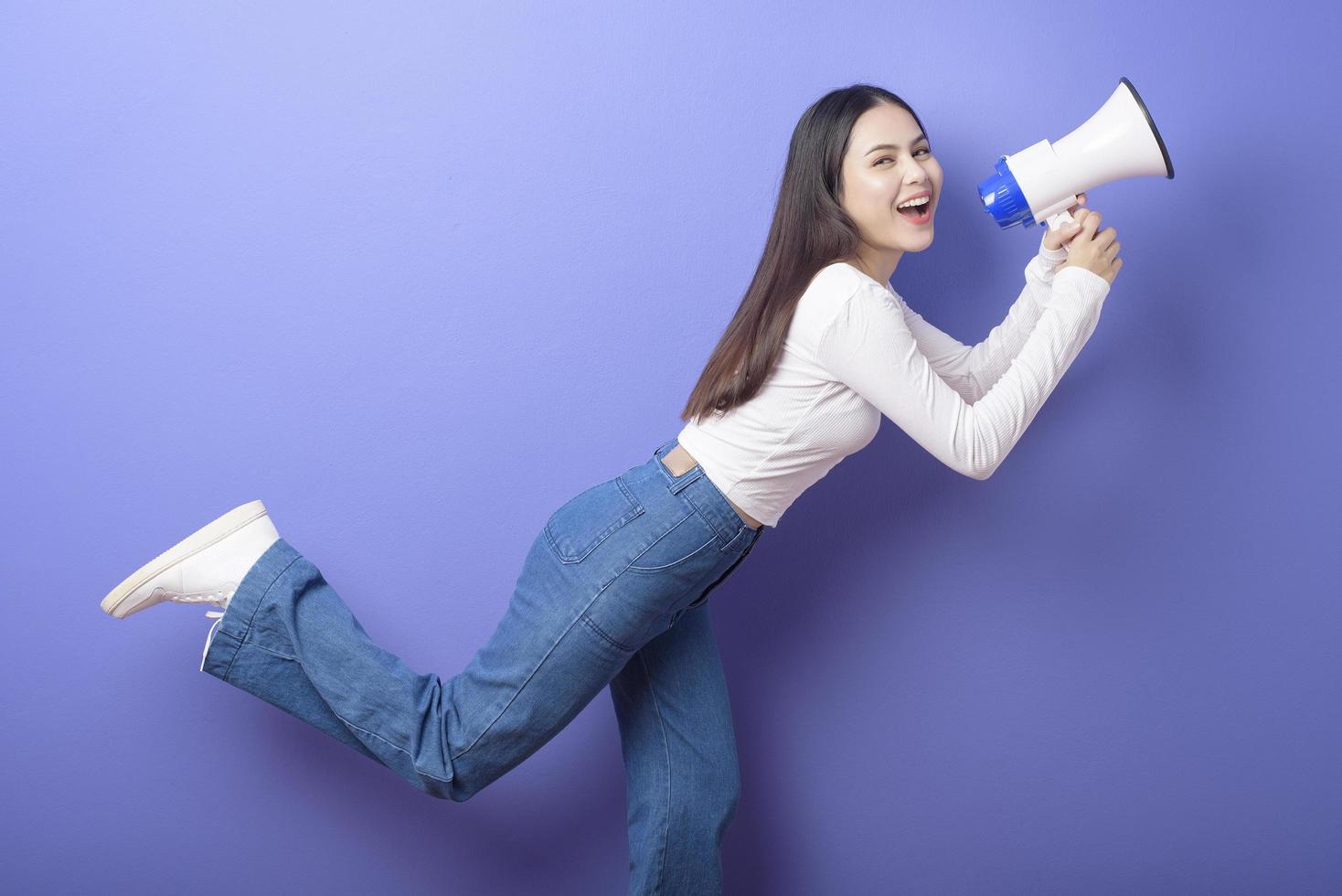 retrato de una joven hermosa mujer sonriente está usando un megáfono para anunciar sobre un estudio aislado de fondo morado foto