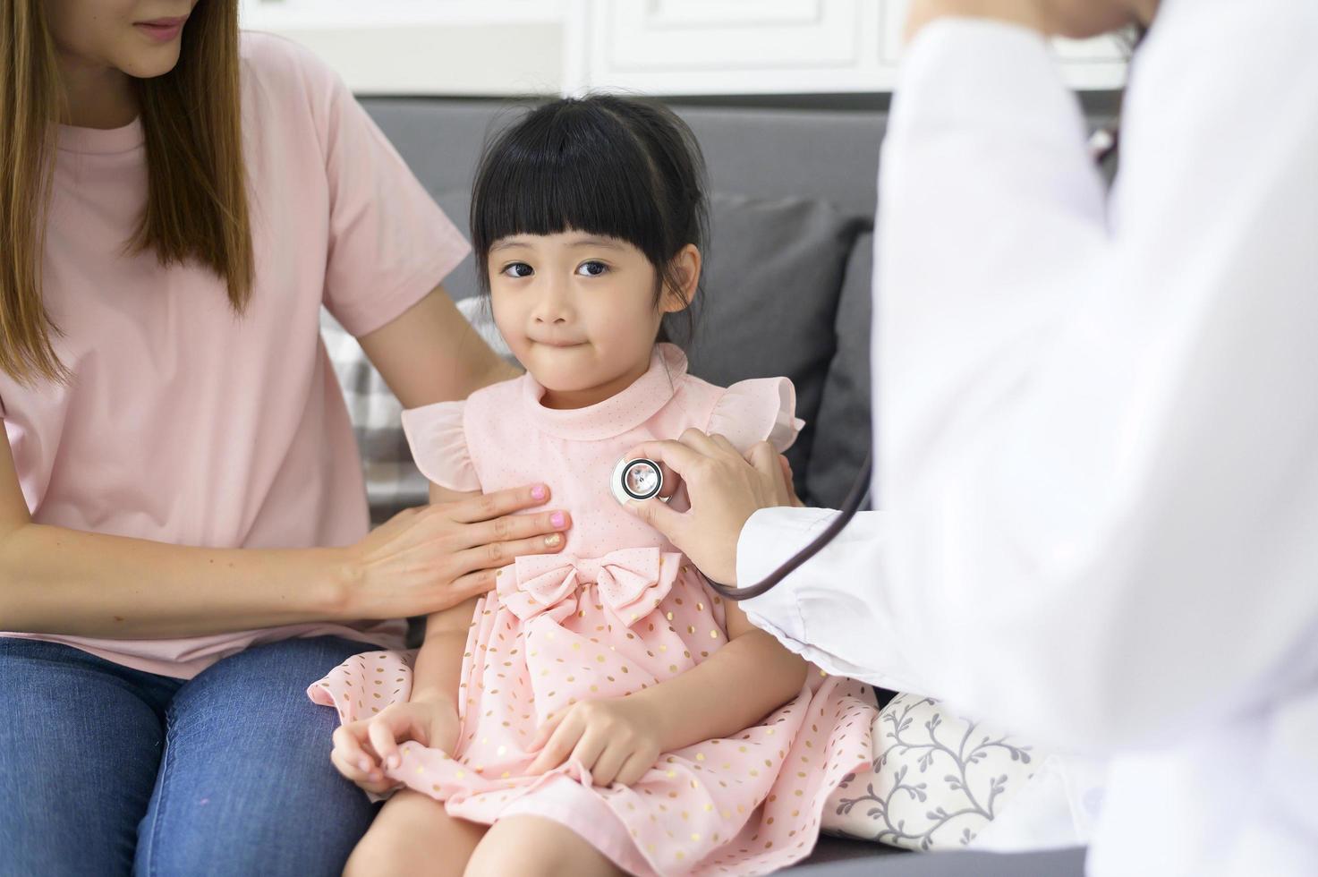 una doctora que sostiene un estetoscopio está examinando a una niña feliz en el hospital con su madre, concepto médico foto