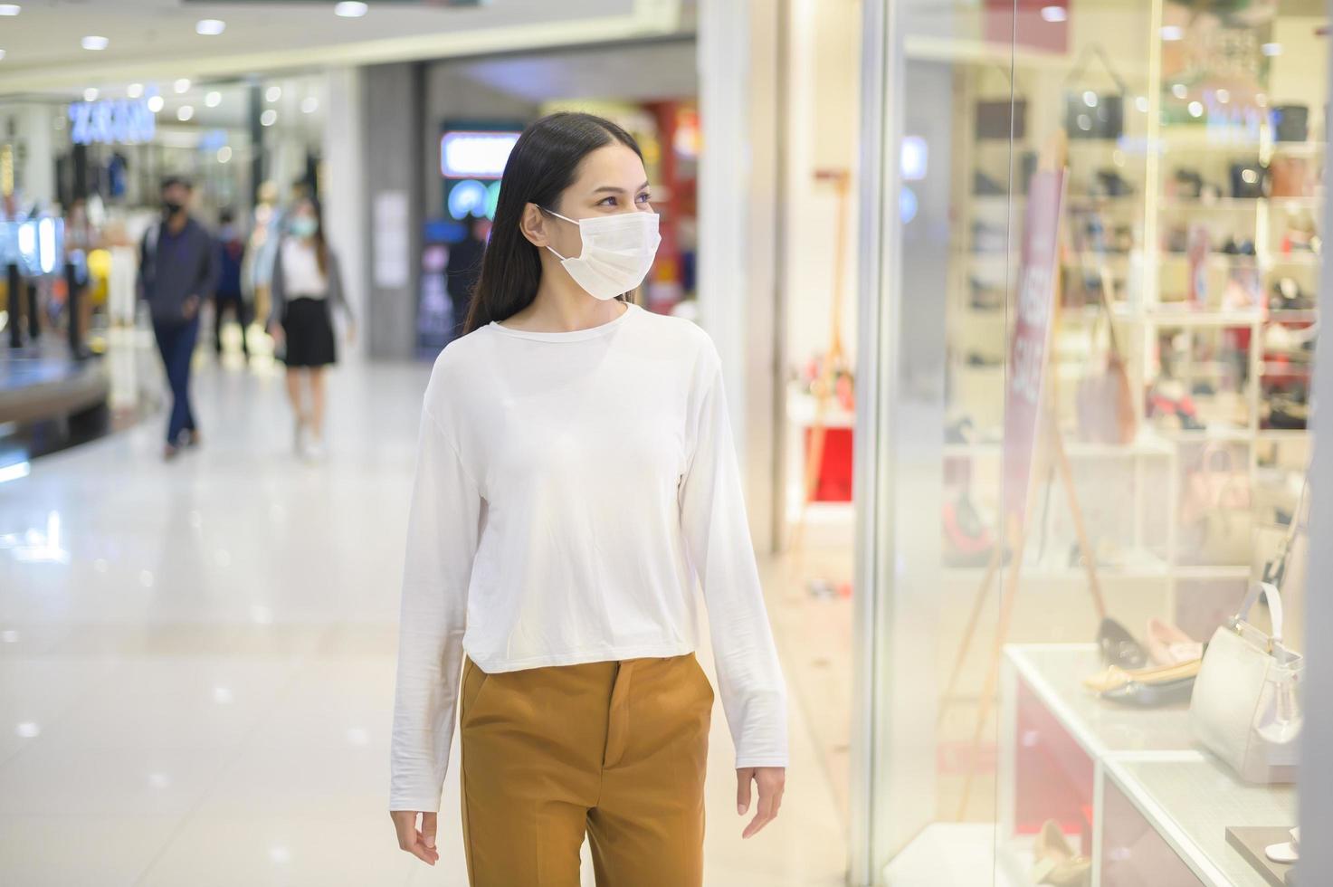 mujer con máscara protectora comprando bajo la pandemia de covid-19 en un centro comercial, protocolo de distanciamiento social, nuevo concepto normal. foto