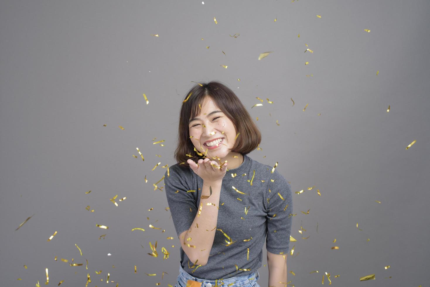 Portrait of young beautiful asian woman celebrating and playing paper shoot isolated gray background studio, Christmas and New Year Concept. photo