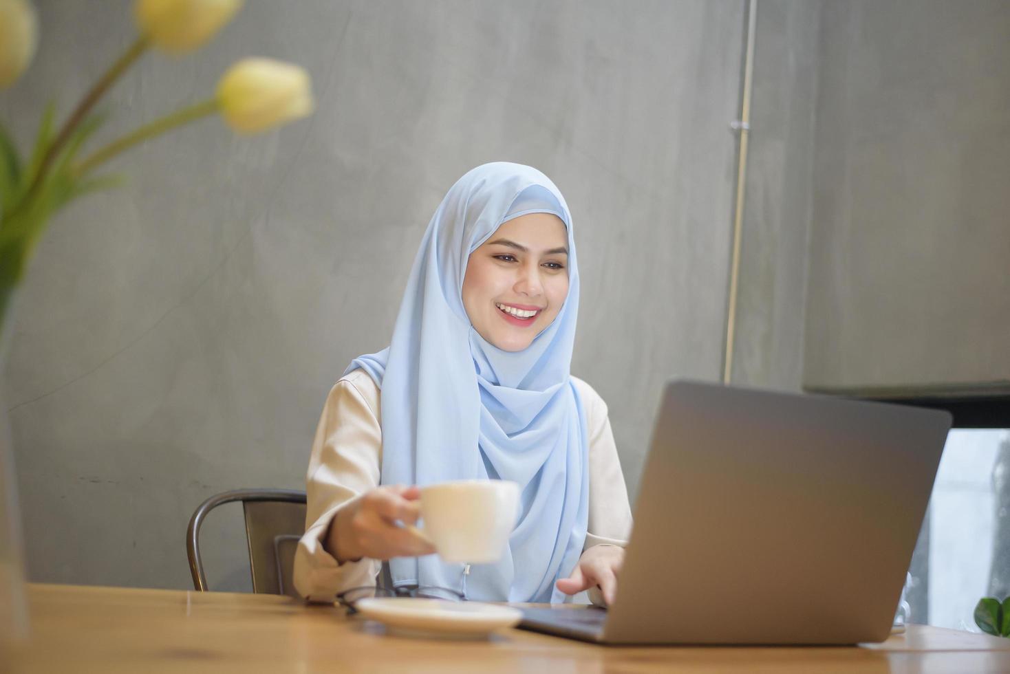 mujer musulmana con hiyab está trabajando con una computadora portátil en una cafetería foto