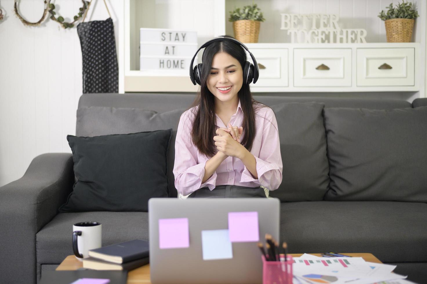 una hermosa joven que usa auriculares está haciendo una videoconferencia a través de una computadora en casa, concepto de tecnología empresarial. foto