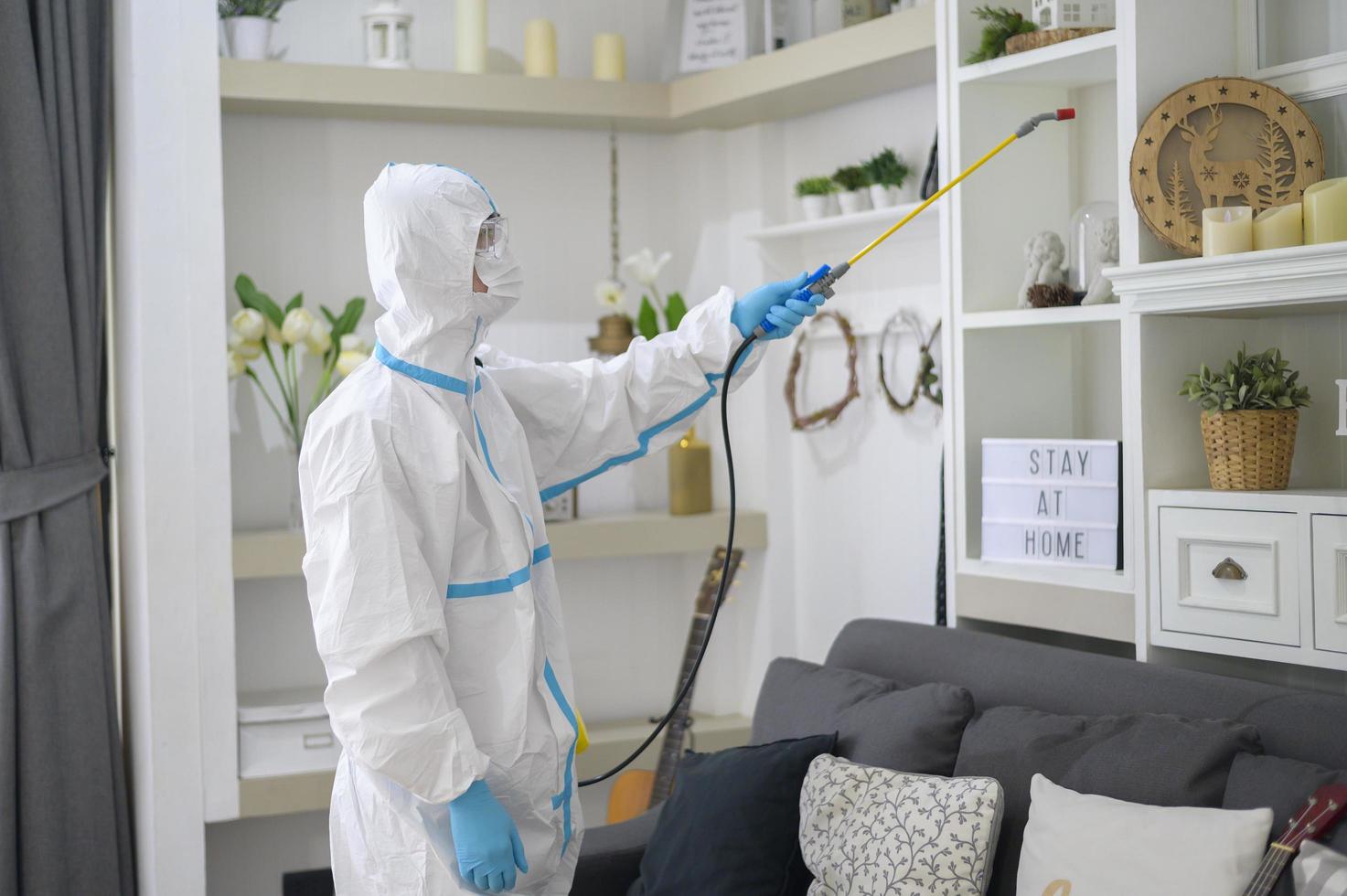 A medical staff in PPE suit is using disinfectant spray in living room, Covid-19 protection , disinfection concept . photo