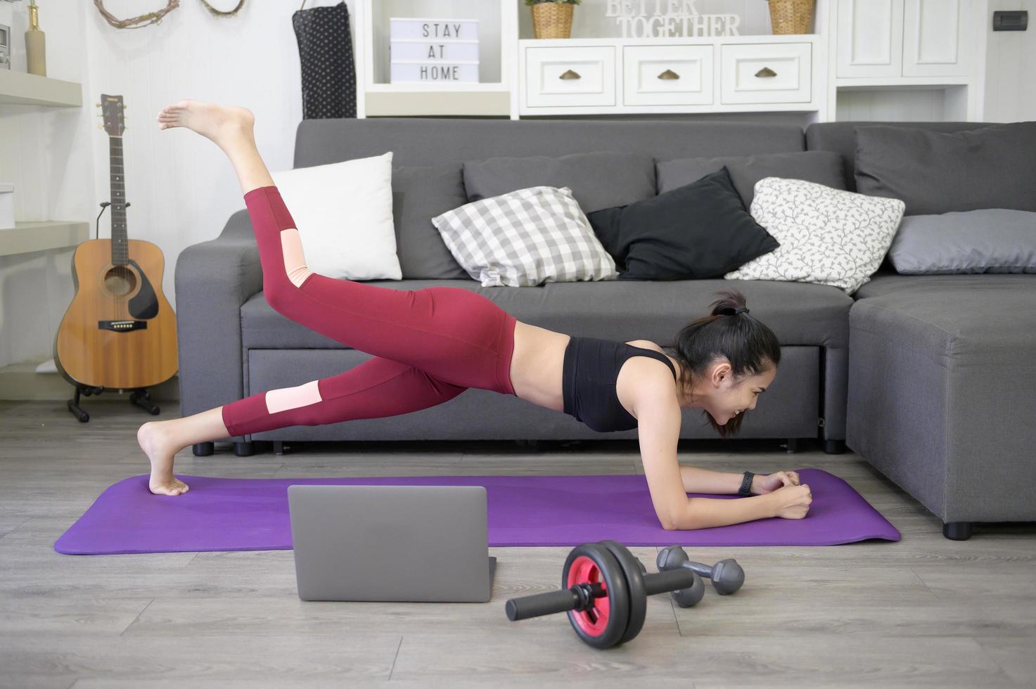 una mujer está haciendo yoga y viendo tutoriales de capacitación en línea en su computadora portátil en la sala de estar, haciendo ejercicio en casa, concepto de tecnología de atención médica. foto