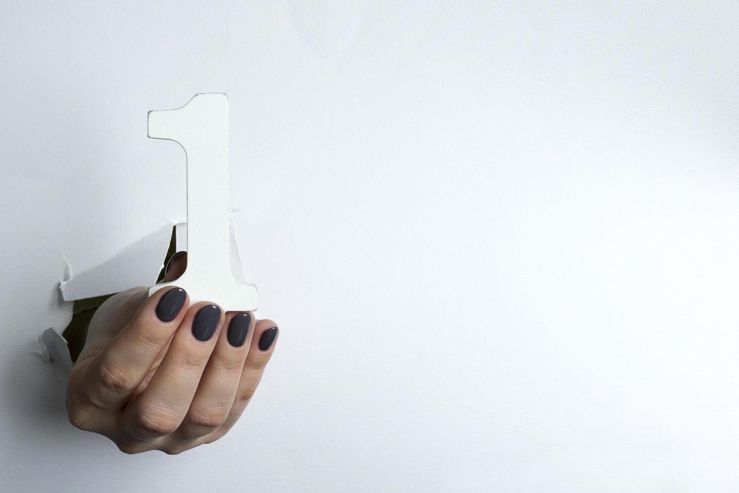 Female hand holding up the number 1 against a white photo