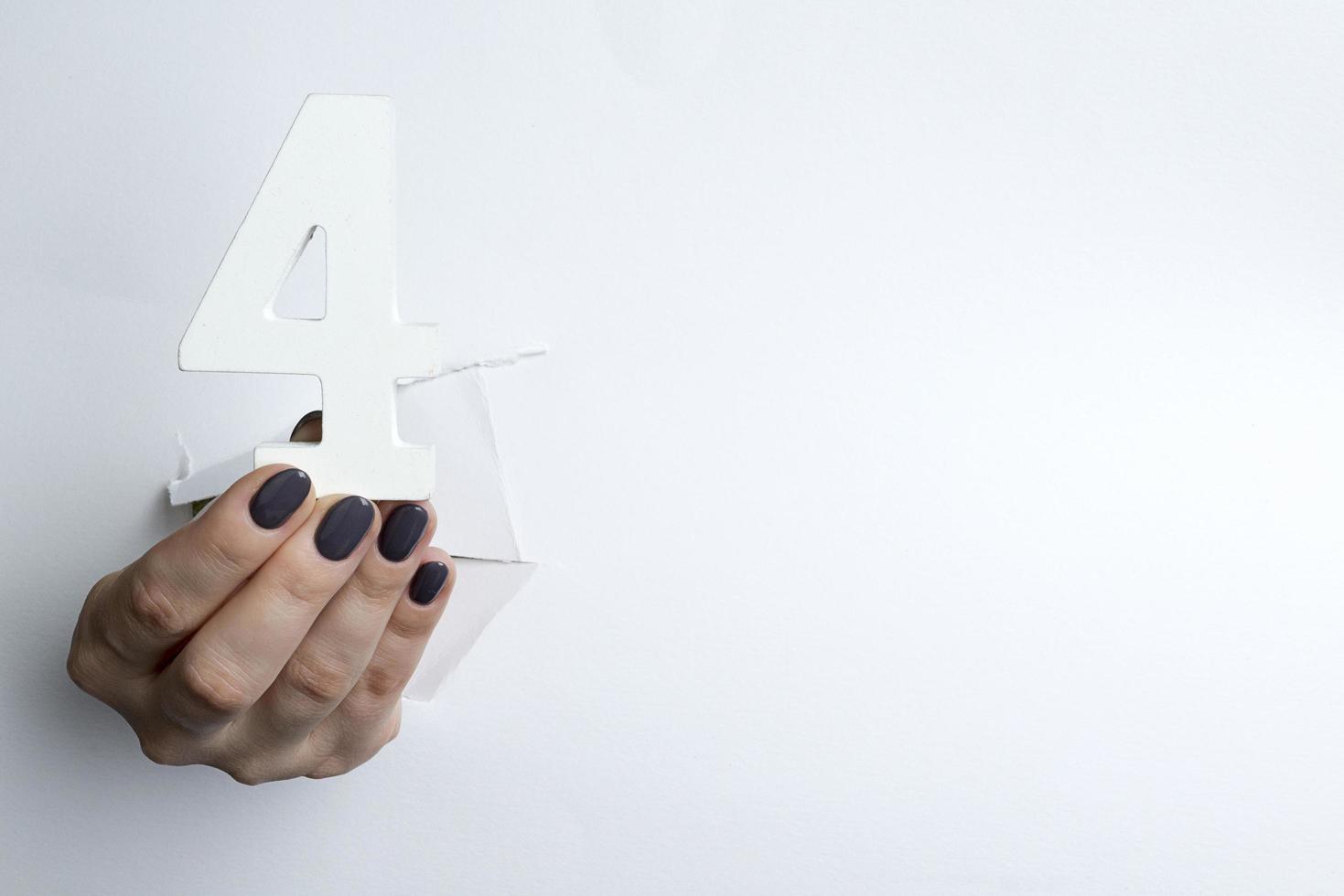 Female hand holding up the number 4 against a white photo