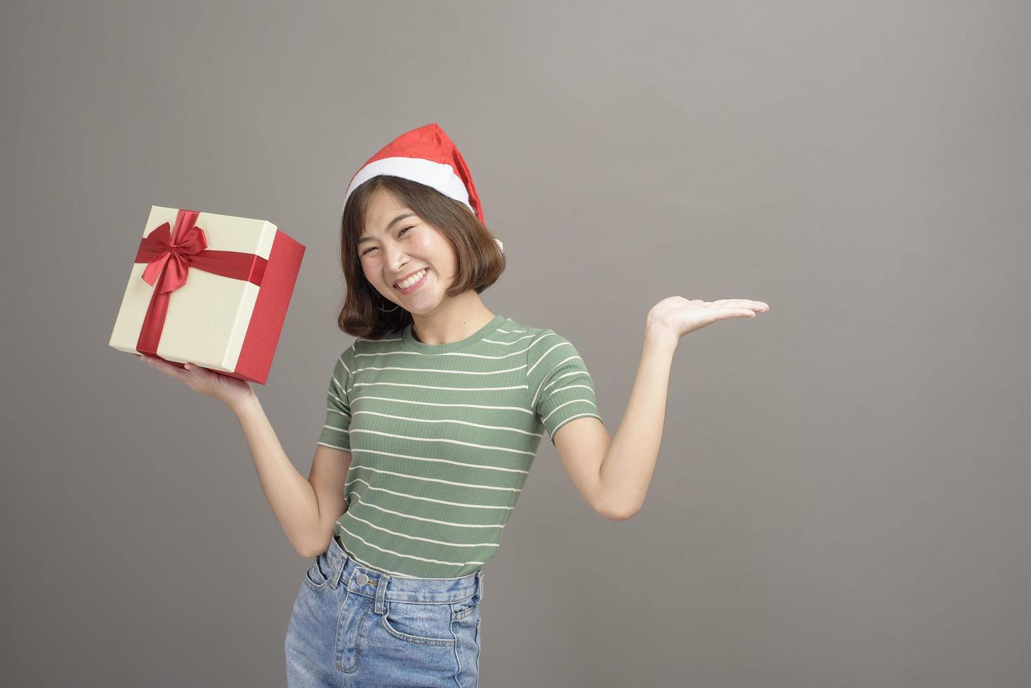 Portrait of beautiful woman wearing red Santa Claus hat holding gift box over studio background, Christmas and New Year Concept photo