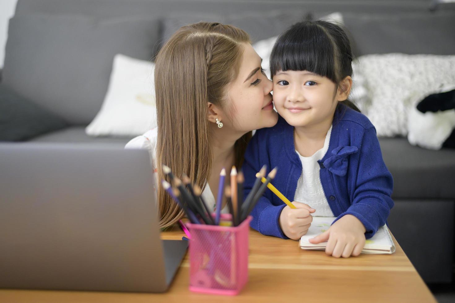 Asian Happy mom and daughter are using laptop for studying online via internet at home. E-learning Concept during quarantine time. photo