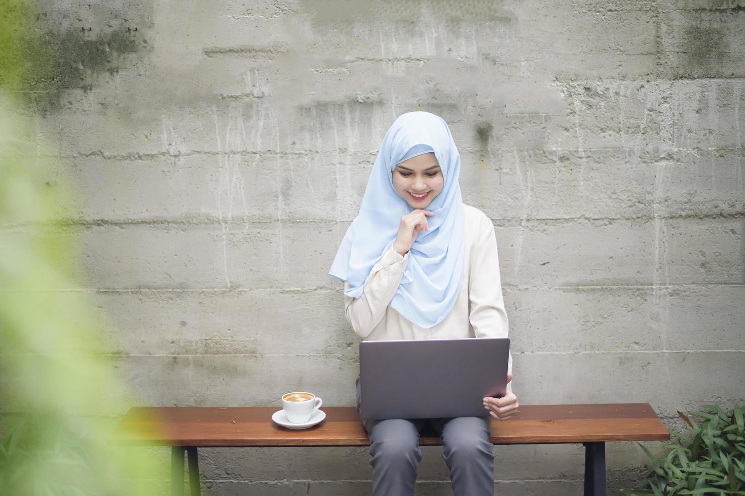 mujer musulmana con hiyab está trabajando con una computadora portátil en una cafetería foto