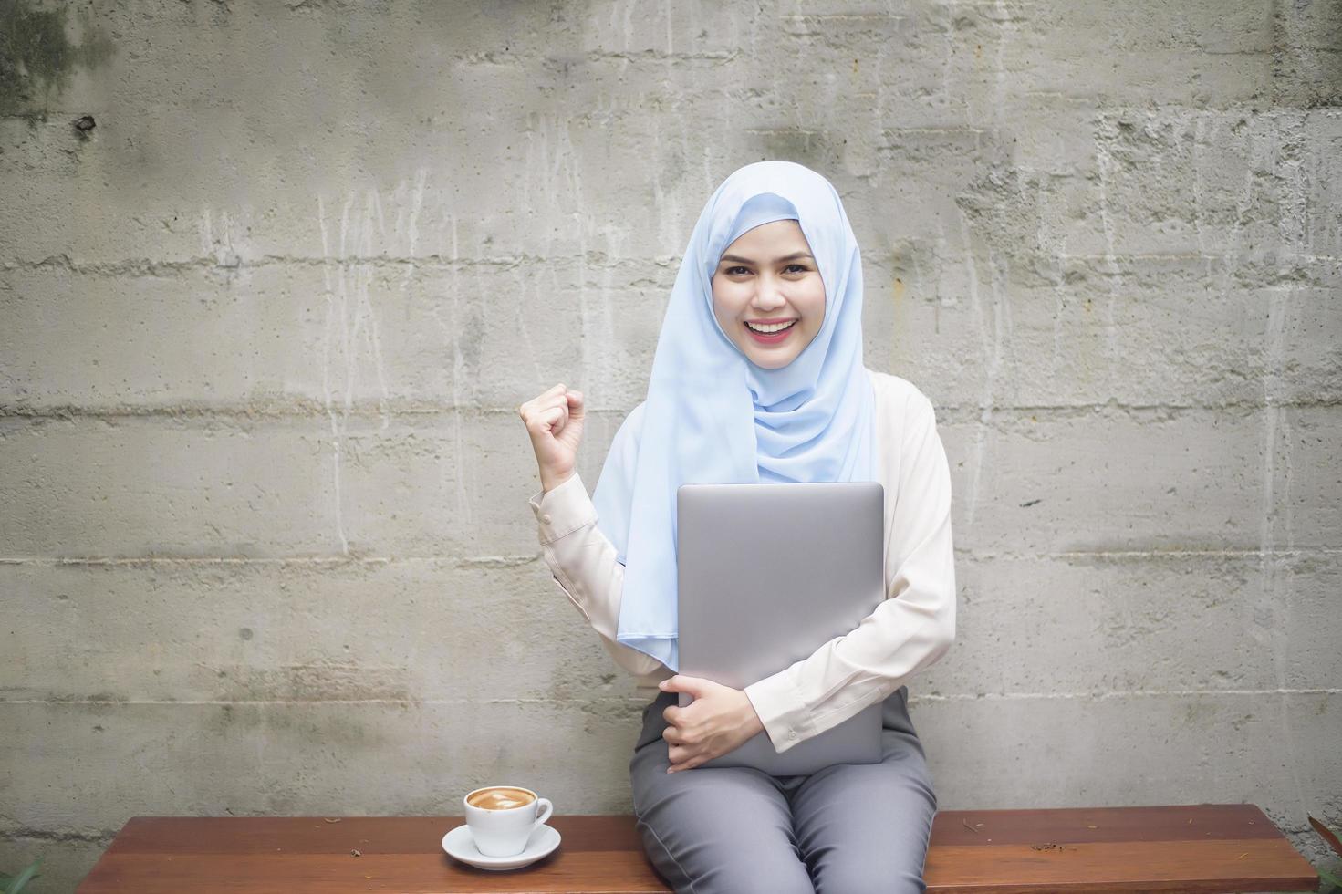 mujer musulmana con hiyab está trabajando con una computadora portátil en una cafetería foto