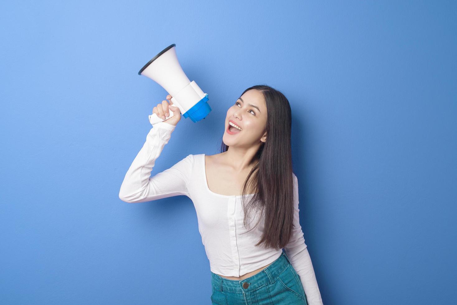 retrato de una joven hermosa mujer sonriente está usando un megáfono para anunciar sobre un estudio de fondo azul aislado foto