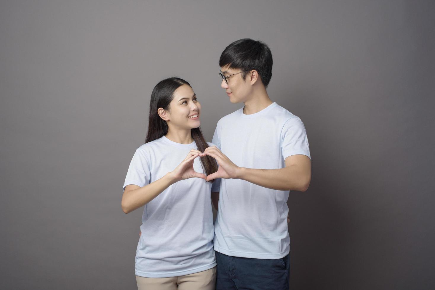 a portriat of a happy couple wearing blue shirt is making  a heart shape with hands over grey background studio photo