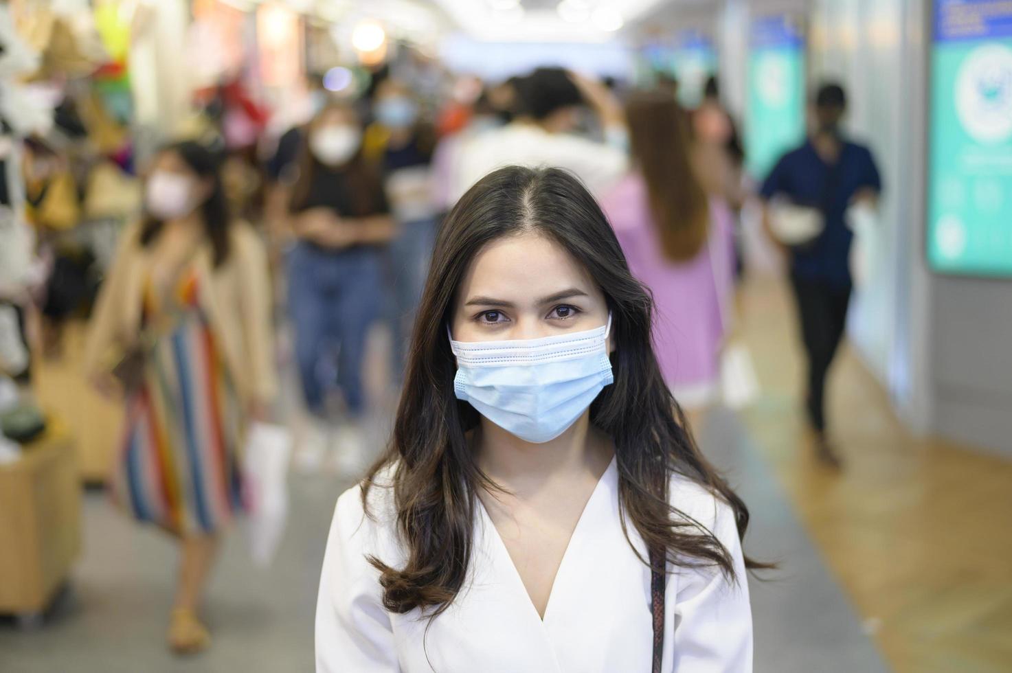 una mujer lleva una máscara protectora en la calle con gente abarrotada mientras la pandemia de covid-19, la protección contra el coronavirus, el concepto de estilos de vida seguros foto