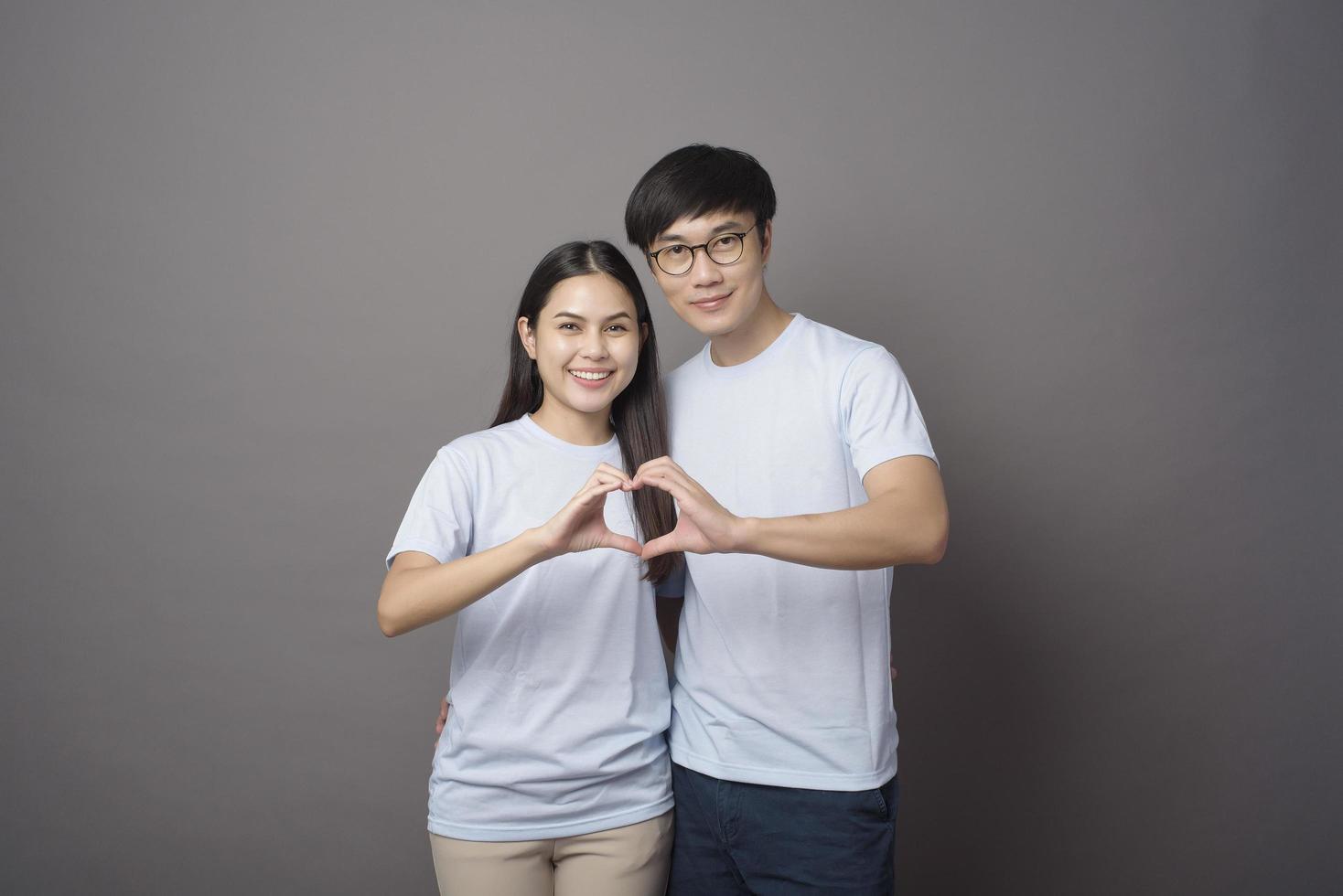 a portriat of a happy couple wearing blue shirt is making  a heart shape with hands over grey background studio photo
