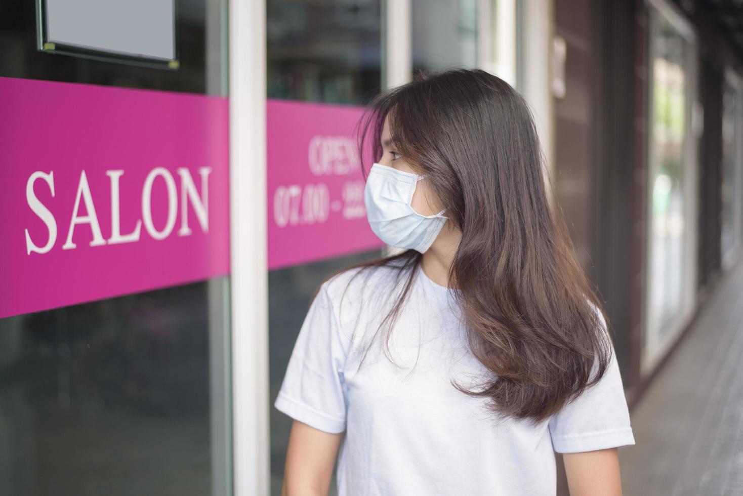a young woman is wearing face mask for protection covid-19 standing in front of Salon shop, salon safety concept photo