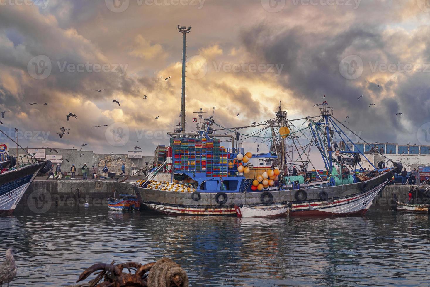 Wooden fishing boats anchored beside pier at marina against cloudy sky photo