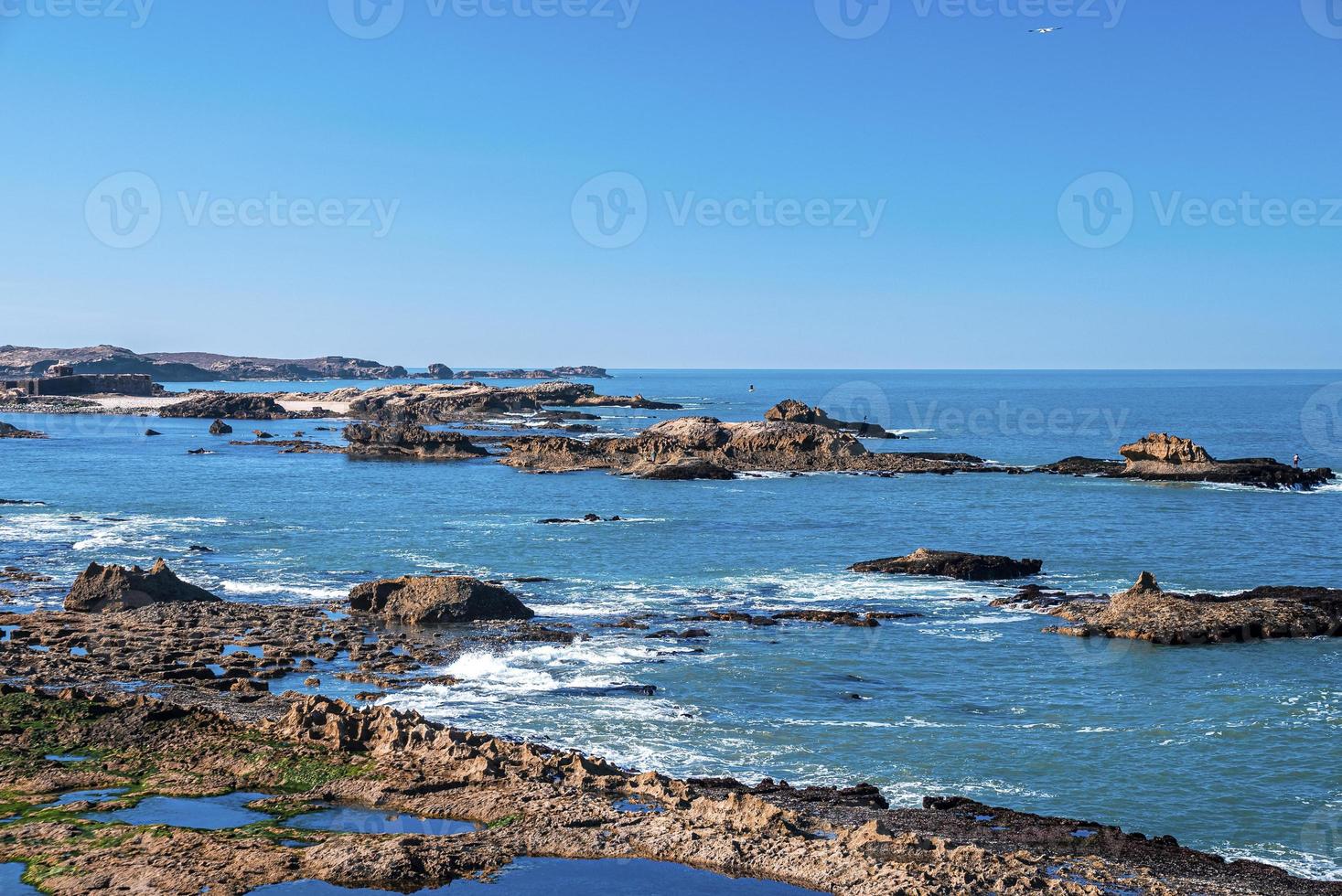 Rock formations at shoreline in sea against blue clear sky photo