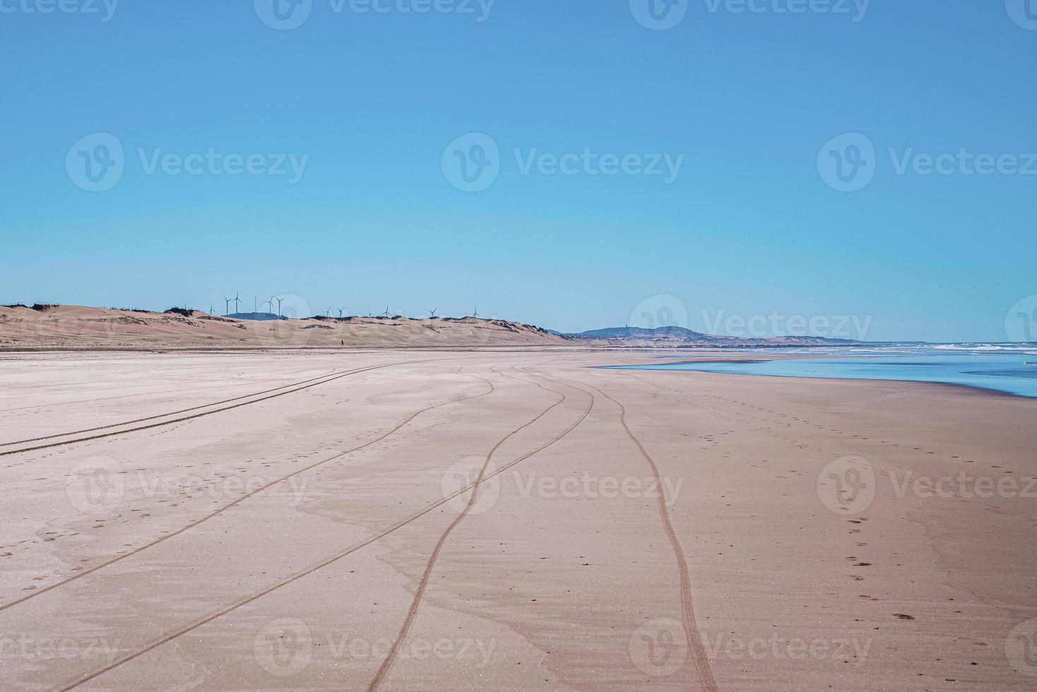 Tyre track and footprints mark on sand with seascape and blue sky photo