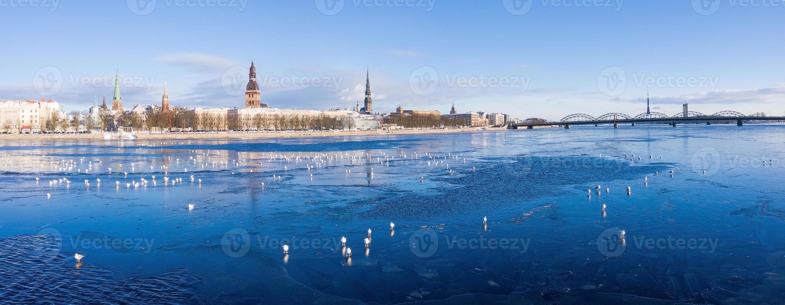 hermosa vista del río congelado con gaviotas sentadas en el hielo junto al casco antiguo de riga en letonia. foto