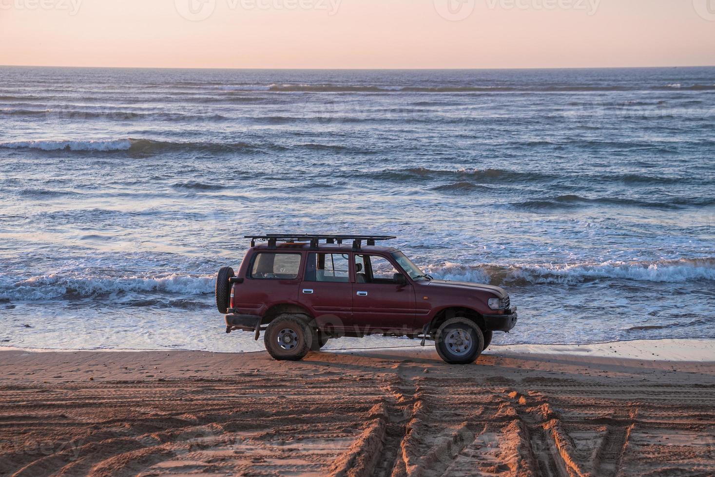 Red offroad car parked at shoreline on sand at beach in evening photo