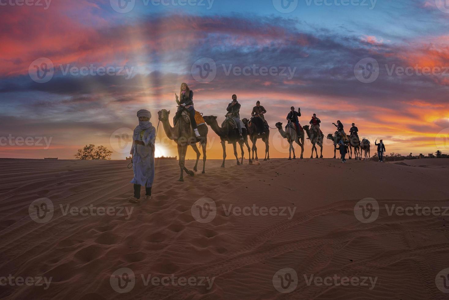 beduino lleva caravana de camellos con turistas a través de la arena en el desierto foto