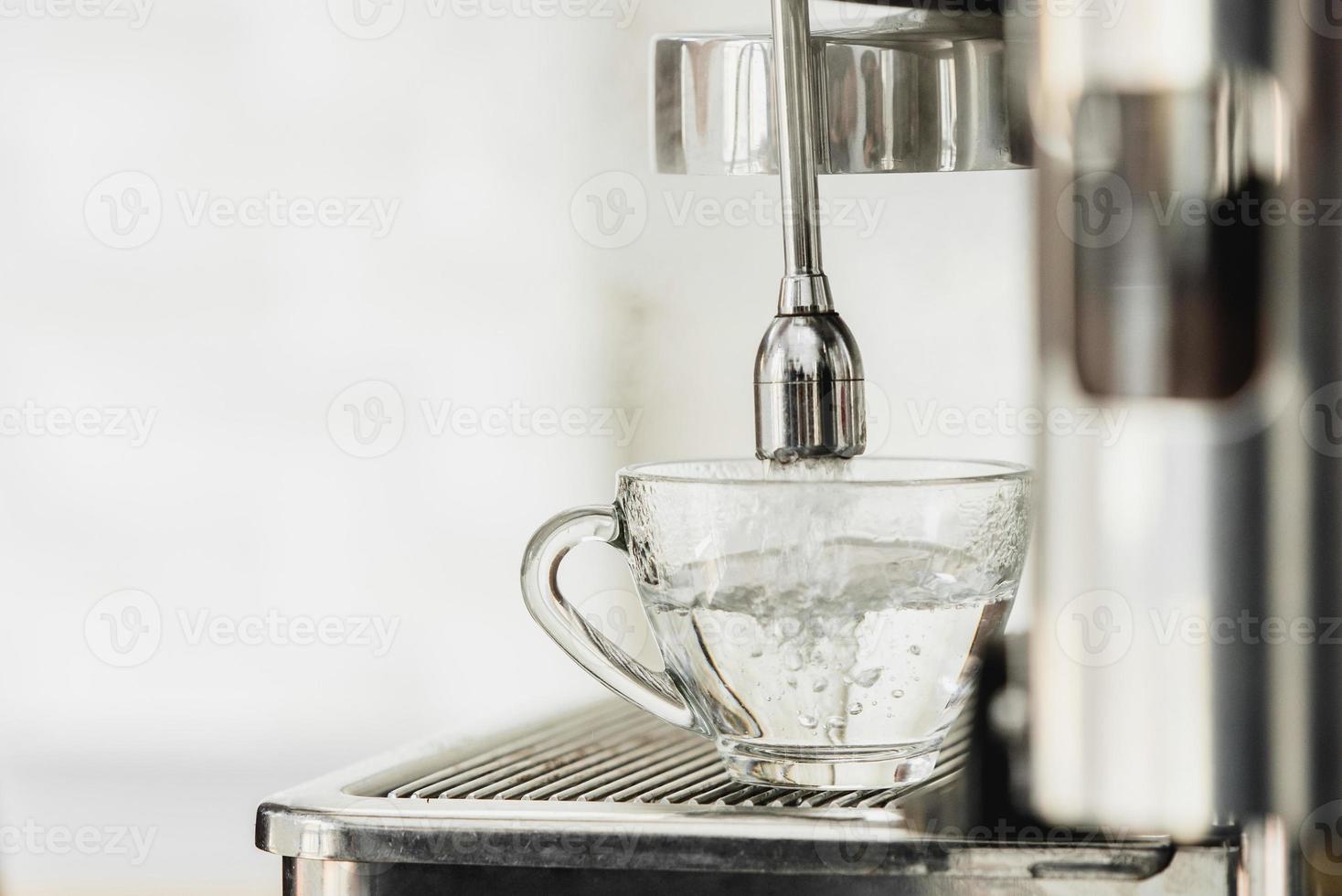 Hot water from coffee maker machine flowing into the cup for Americano making photo