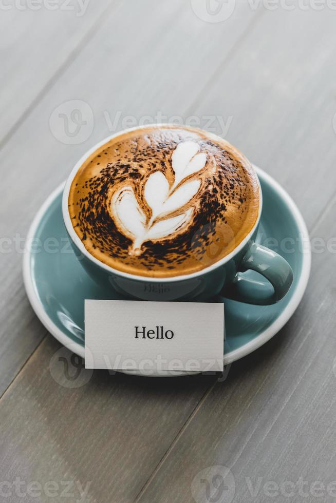 taza de café con arte latte y hola texto de saludo en la mesa de madera foto