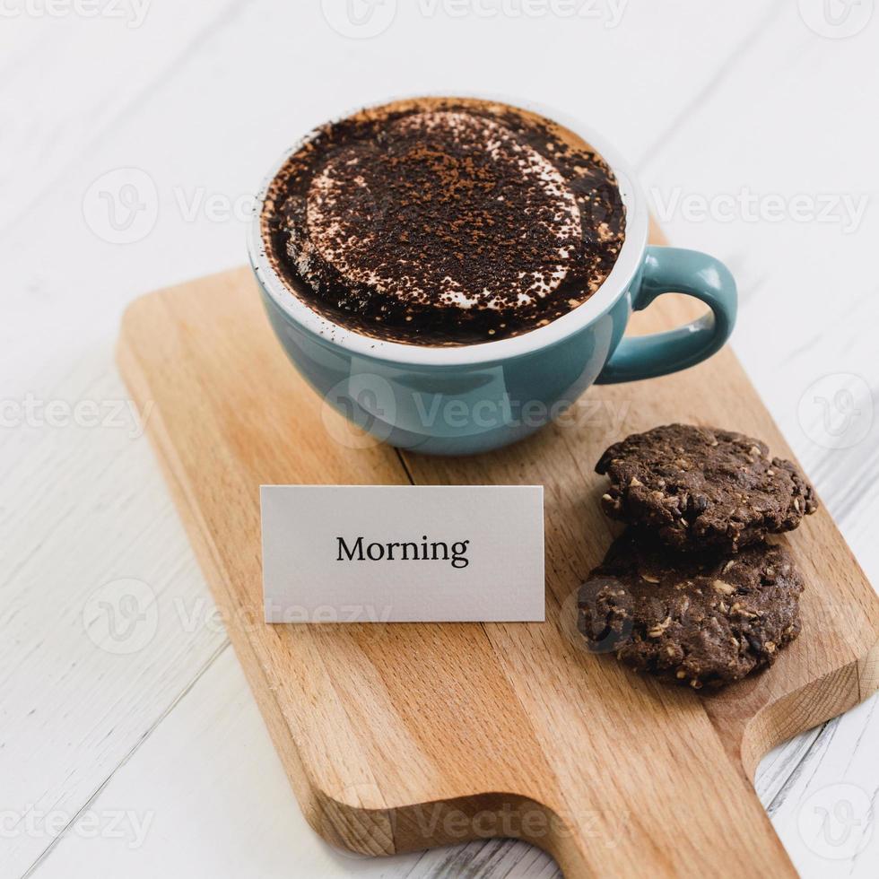 Cup of coffee with dark chocolate cookies and greeting message on wood platter in cafe photo