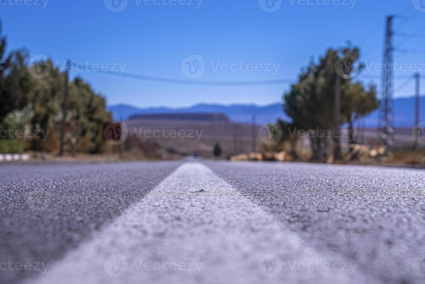 Carretera asfaltada recta con marcas de superficie blanca contra montañas en segundo plano. foto