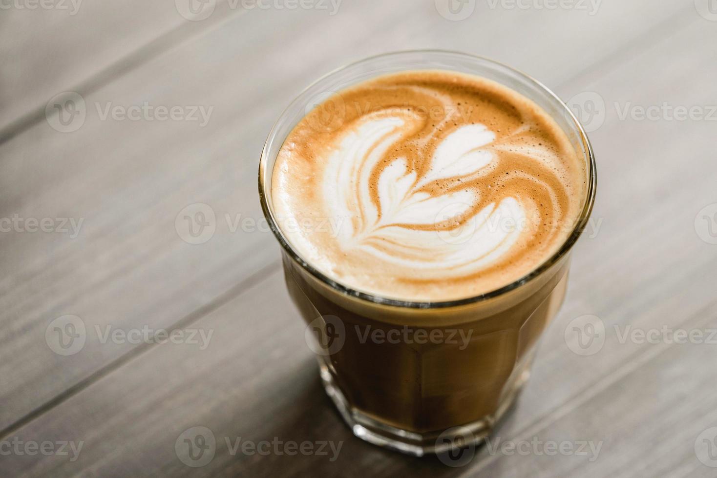 Close up of fresh brewed coffee in tumbler glass with beautiful latte art on wooden table background photo