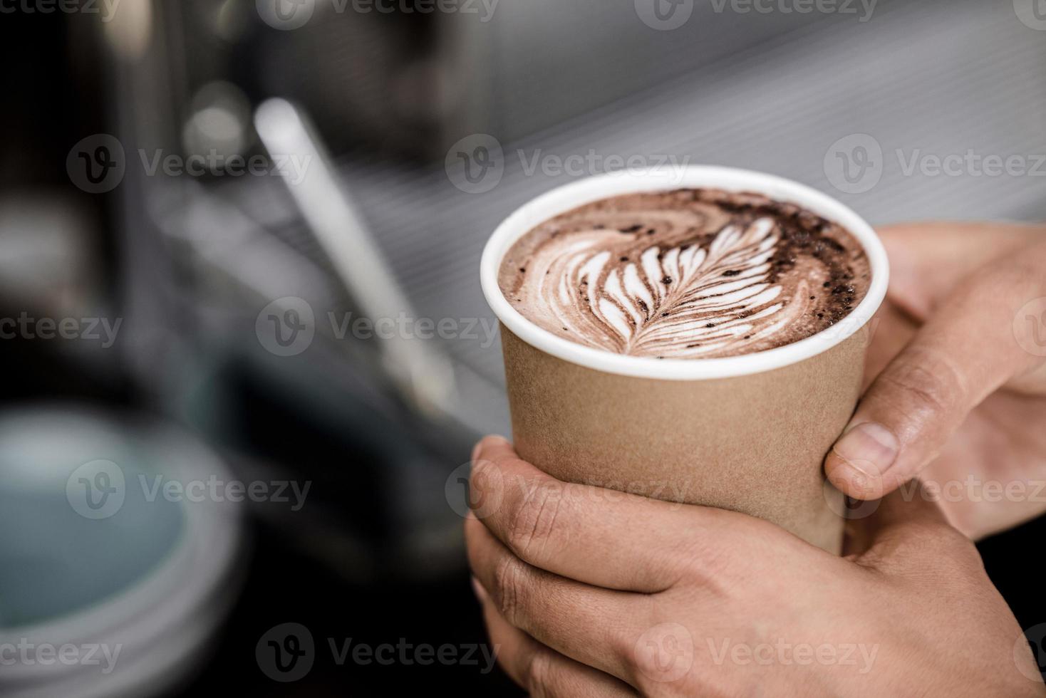 primer plano de manos masculinas sosteniendo una taza de café caliente preparado con diseño de arte de helecho latte foto