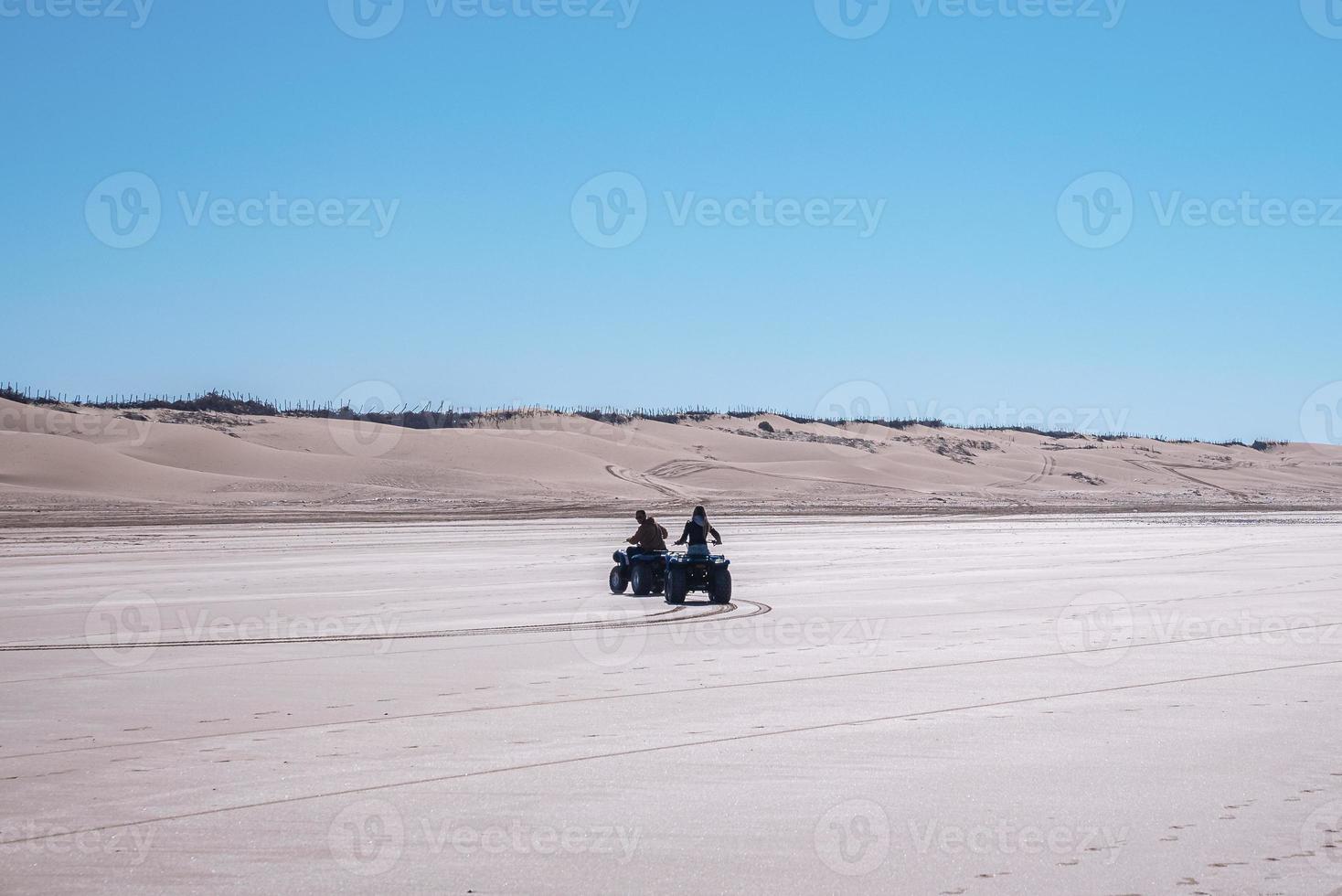 People riding quad bikes through sandy road along with sand dunes photo