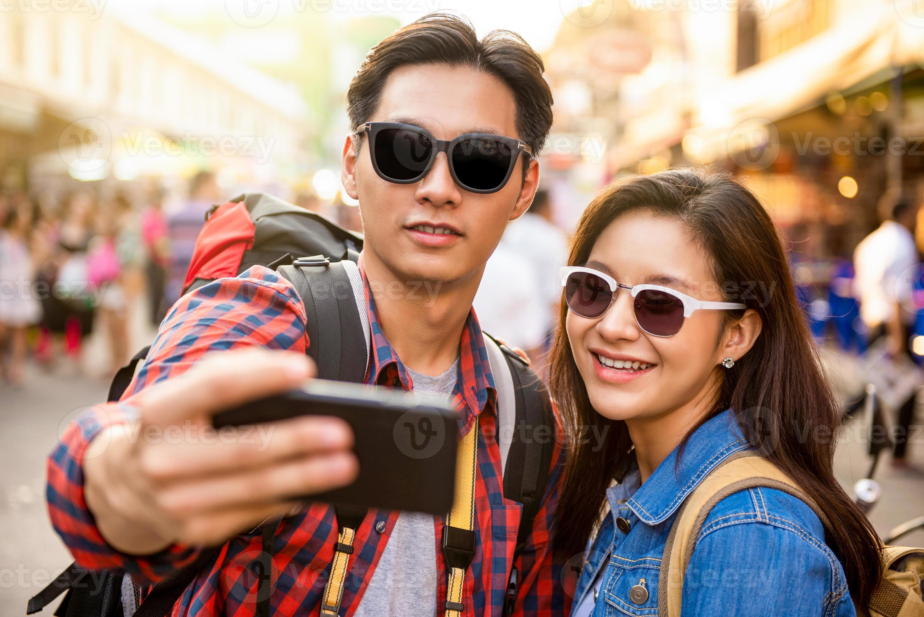 Smiling young Asian couple tourists taking selfie while traveling in Khao San road Bangkok Thailand during summer vacation photo