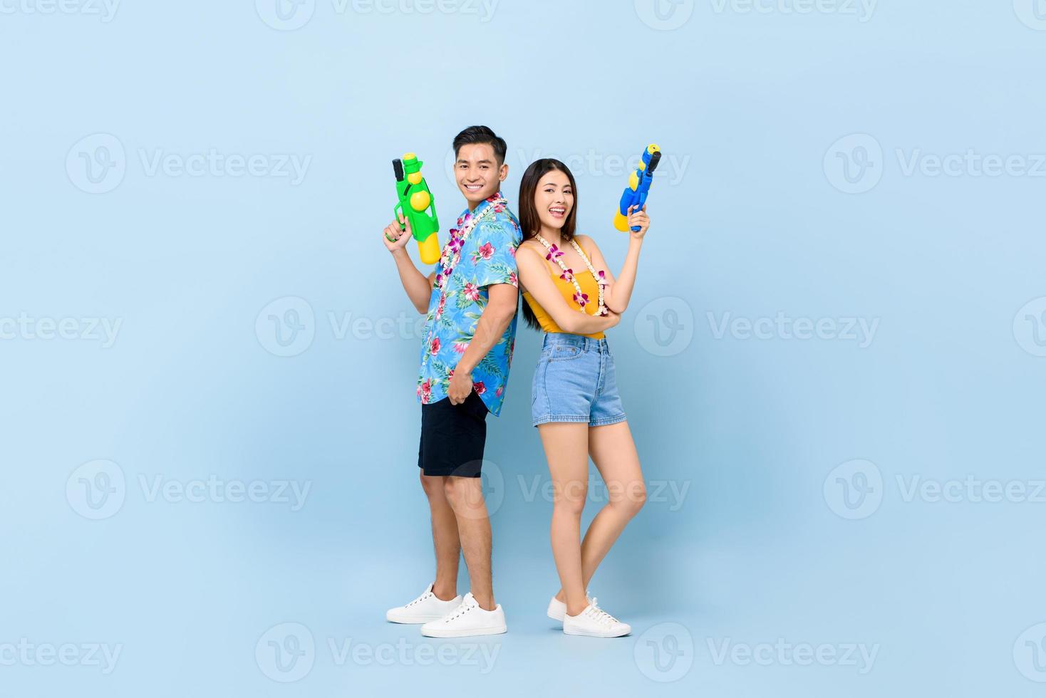 Young Asian couple in summer outfits with water guns in studio blue background for Songkran festival in Thailand and southeast Asia photo